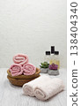 Clean pink towels stacked with a houseplant on a white table, shampoo, conditioner, and soap beside, with room for text. 138404340