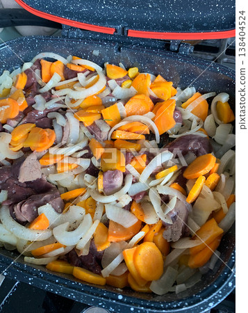 Vegetables including carrots, beets, and garlic are prepared on a baking tray ready to bake in the oven. The tray is lined and set on a stove surface 138404524