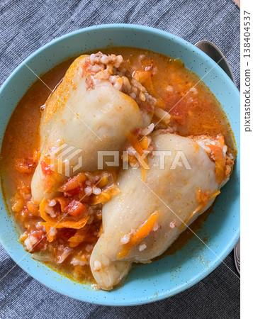 Cabbage rolls filled with meat and grains sit in a blue bowl. The dish is covered in a rich tomato sauce. It is ready to be enjoyed at dinner time in a warm kitchen 138404537