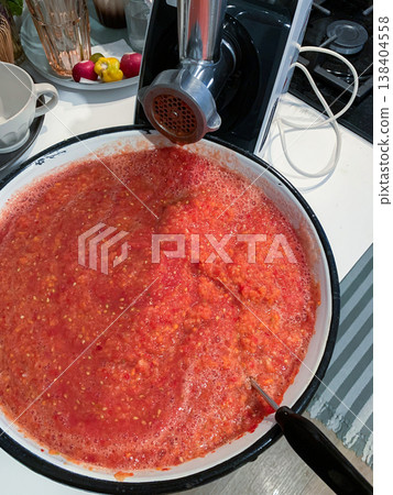 Tomatoes are being ground into a thick sauce in a kitchen. A food grinder is set up on the counter. Other colorful ingredients are on display Tomatoes are being ground into a thick sauce in a kitchen. A food grinder is set up on the counter. Other colorful ingredients are on display 138404558