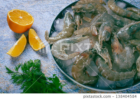 Fresh raw shrimp spread on ice with lemon and cilantro slices on a marble surface, ready to cook, no people Fresh raw shrimp spread on ice with lemon and cilantro slices on a marble surface, ready to cook, no people 138404584