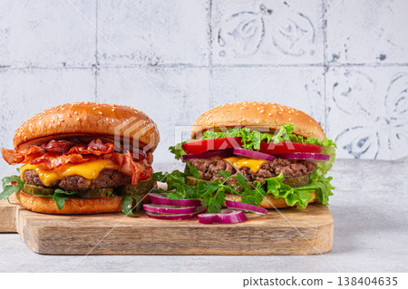 two burgers with beef patty, fried bacon, cheddar cheese, tomatoes, on a light table, two burgers with beef patty, fried bacon, cheddar cheese, tomatoes, on a light table, 138404635