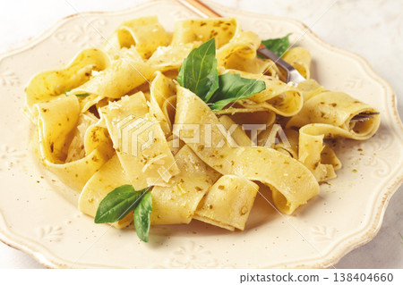 Fresh papardelle pasta, with basil and pesto sauce, is served, on a white plate, with a fork held by hand Fresh papardelle pasta, with basil and pesto sauce, is served, on a white plate, with a fork held by hand 138404660