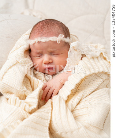 Portrait of a sleeping newborn baby wrapped in a soft knitted beige blanket. Minimal newborn photography with gentle light, calm mood, warmth, tenderness and early family lifestyle concept 138404759