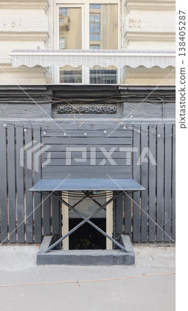 Black folding table with crossed legs positioned against a wooden fence, featuring a window with white curtains above and decorative molding on the wall 138405287