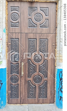 Decorative wooden door with intricate carvings and keypad lock, surrounded by a textured wall and blue paint, showcasing urban architectural details Decorative wooden door with intricate carvings and keypad lock, surrounded by a textured wall and blue paint, showcasing urban architectural details 138405308