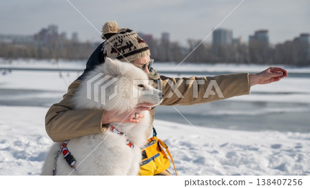 Smiling woman holding fluffy samoyed dog in snowy winter park.  138407256