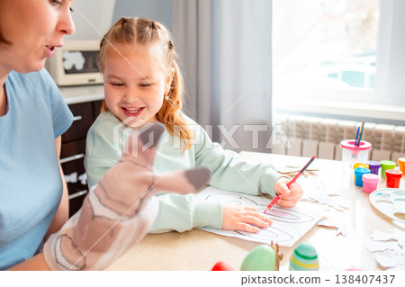 A Caucasian woman and her daughter decorate paper bunny masks at the table, enjoying creative Easter preparation and family bonding. Mid shot A Caucasian woman and her daughter decorate paper bunny masks at the table, enjoying creative Easter preparation and family bonding. Mid shot 138407437