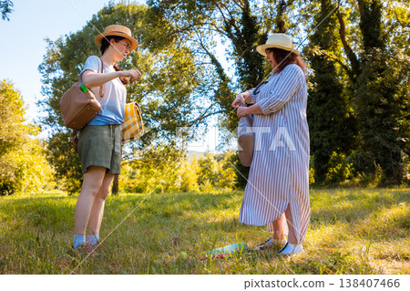 Mother and daughter Caucasian walking in summer park holding blanket looking for a picnic spot having fun and spending quality outdoor family time together. Low angle view Mother and daughter Caucasian walking in summer park holding blanket looking for a picnic spot having fun and spending quality outdoor family time together. Low angle view 138407466