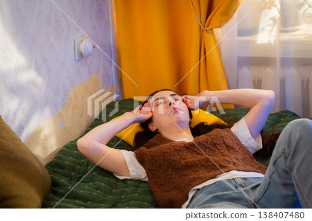 Woman sits on bed in softly lit room holding VR glasses away from face, showing discomfort. Realistic reaction to digital interaction and new tech exploration. Woman sits on bed in softly lit room holding VR glasses away from face, showing discomfort. Realistic reaction to digital interaction and new tech exploration. 138407480