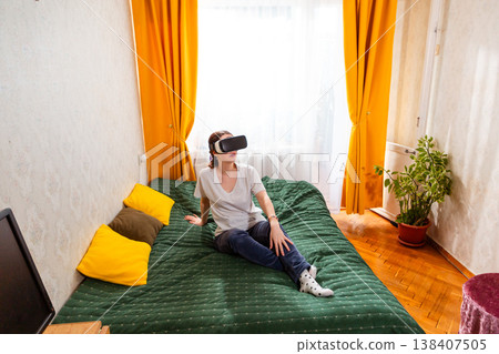 Woman interacting with virtual reality spaces while sitting on bed, embracing the evolution of digital entertainment. Wide shot, top view Woman interacting with virtual reality spaces while sitting on bed, embracing the evolution of digital entertainment. Wide shot, top view 138407505