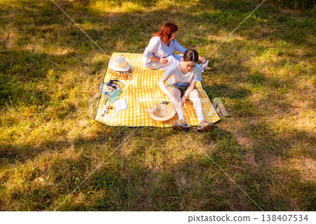 Picnic in summer park with two women showing visible discomfort due to insect bites while sitting on yellow mat and enjoying nature together. Top view Picnic in summer park with two women showing visible discomfort due to insect bites while sitting on yellow mat and enjoying nature together. Top view 138407534