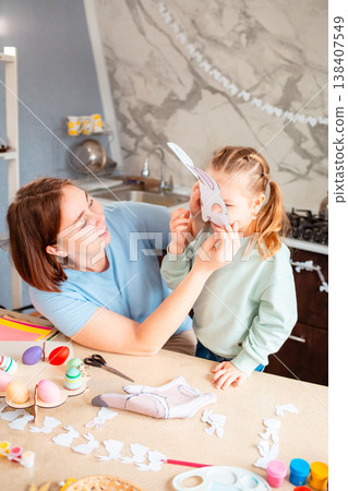 A beautiful family moment as a mother and her daughter wear Easter bunny masks at home, enjoying playful crafting time before the holiday celebration. Vertical A beautiful family moment as a mother and her daughter wear Easter bunny masks at home, enjoying playful crafting time before the holiday celebration. Vertical 138407549