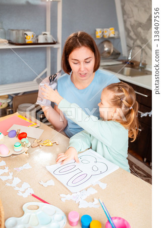 A Caucasian woman and her daughter craft holiday ornaments together, cutting decorations at the table and celebrating Easter traditions with children. Vertical A Caucasian woman and her daughter craft holiday ornaments together, cutting decorations at the table and celebrating Easter traditions with children. Vertical 138407556