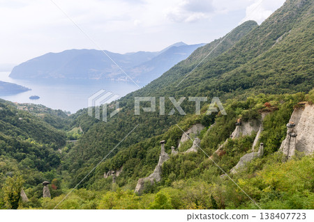 Panoramic hillside scene of the Pyramids of Zone with Lake Iseo behind white hoodoos Panoramic hillside scene of the Pyramids of Zone with Lake Iseo behind white hoodoos 138407723