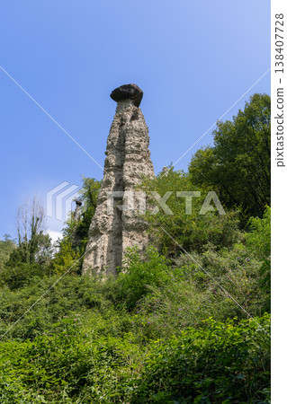 Low angle view of giant capped hoodoo at the Pyramids of Zone with pale tower and blue sky in Italy 138407728