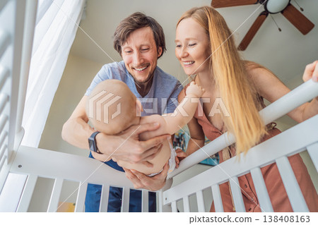 Mother and father lifting baby from crib and holding in arms at home. Loving parents caring for newborn together. Family bonding, parenthood, tenderness and emotional connection concept Mother and father lifting baby from crib and holding in arms at home. Loving parents caring for newborn together. Family bonding, parenthood, tenderness and emotional connection concept 138408163