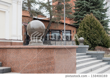 Ornate Granite Sphere Decorative Finials Adorning Reddish-Brown Stone Wall With Gray Steps Near Brick Building And Evergreen Trees In Overcast Outdoor Setting 138408169