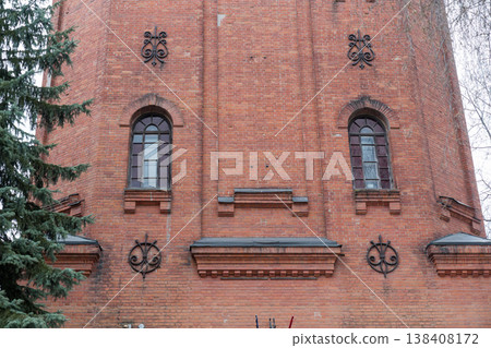 Historic Red Brick Church Tower With Ornate Iron Decorations And Arched Windows Set Against Overcast Sky In Urban Park Setting Historic Red Brick Church Tower With Ornate Iron Decorations And Arched Windows Set Against Overcast Sky In Urban Park Setting 138408172