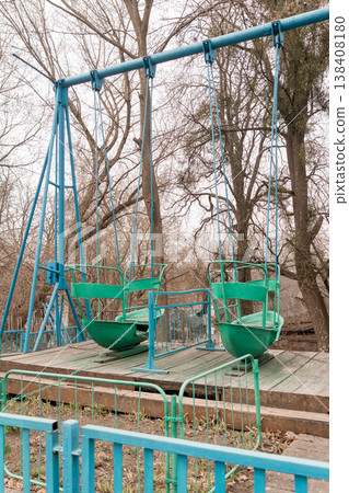 Vintage Blue and Green Swing Set in Abandoned Park with Bare Trees and Weathered Wooden Platform Showing Signs of Decay Vintage Blue and Green Swing Set in Abandoned Park with Bare Trees and Weathered Wooden Platform Showing Signs of Decay 138408180
