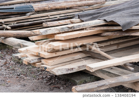 Weathered Wooden Planks Piled Outdoors Under Grey Tarp with Natural Textures and Rustic Building Materials Display 138408194