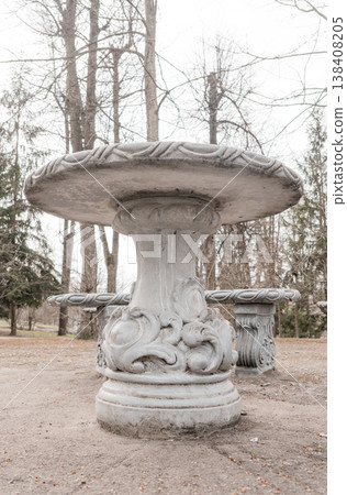 Weathered Gray Stone Garden Table With Ornate Carvings And Matching Bench In Quiet Leafless Forest Setting During Overcast Day 138408205