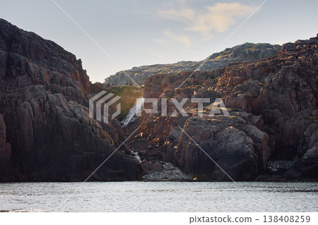 Russia, Teriberka, many people admire the waterfall at the edge of the Battery waterfall at sunet, Arctic landscape with a view of a flowing waterfall in the northern fjord 138408259