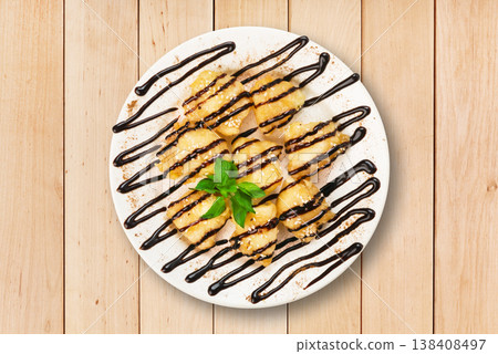 A round plate displays a dessert topped with chocolate drizzle and a sprig of mint. The plate is set on a wooden table, highlighting the dessert's features. 138408497