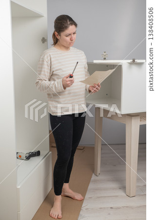 A Caucasian woman looks at the assembly instructions for a wardrobe with confusion. 138408506