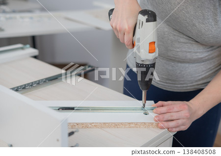 A Caucasian woman uses a screwdriver to tighten a screw while assembling a cabinet. 138408508