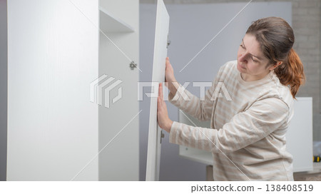A Caucasian woman assembles a wardrobe. A Caucasian woman assembles a wardrobe. 138408519