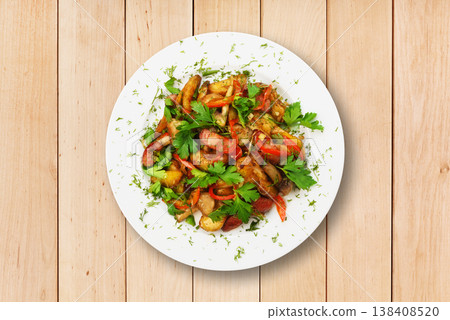 A plate contains a mix of vegetables and herbs, featuring greens and reds. The food is arranged on a white dish and set on a wooden table surface. 138408520