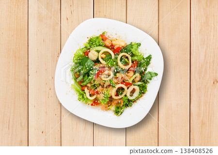 A bowl contains a mix of greens, diced tomatoes, nuts, and onions. The bowl sits on a simple wooden table. There are no utensils or beverages present in the setting. A bowl contains a mix of greens, diced tomatoes, nuts, and onions. The bowl sits on a simple wooden table. There are no utensils or beverages present in the setting. 138408526