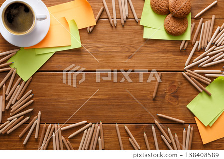 Top view on work space with stationery. Coffee break at office workplace. Assortment of pencils and colored memo stickers making frame for copy space on wooden table Top view on work space with stationery. Coffee break at office workplace. Assortment of pencils and colored memo stickers making frame for copy space on wooden table 138408589