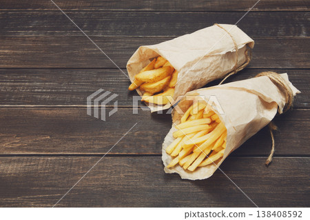 Tasty potato wedges and french fries wrapped into brown kraft wrapping paper. Fast food take away at rustic wood background. Choice of fried potatoes at wood. Chips, potato slices. Top view, copyspace Tasty potato wedges and french fries wrapped into brown kraft wrapping paper. Fast food take away at rustic wood background. Choice of fried potatoes at wood. Chips, potato slices. Top view, copyspace 138408592