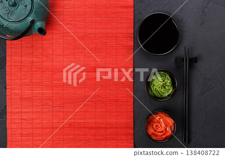 Table set for traditional japanese dinner. Black saucer with soy sauce, ginger and wasabi in small plates, chopsticks and teapot on red bamboo mat. Flat lay, copy space, background Table set for traditional japanese dinner. Black saucer with soy sauce, ginger and wasabi in small plates, chopsticks and teapot on red bamboo mat. Flat lay, copy space, background 138408722