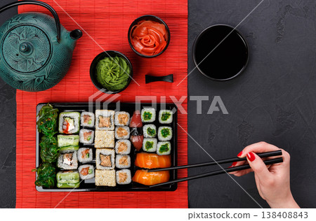 Eating salmon sushi in japanese restaurant, hand with chopsticks top view. Female has dinner, top view on black Eating salmon sushi in japanese restaurant, hand with chopsticks top view. Female has dinner, top view on black 138408843