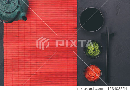 Table set for traditional japanese dinner. Black saucer with soy sauce, ginger and wasabi in small plates, chopsticks and teapot on red bamboo mat. Flat lay, copy space, background Table set for traditional japanese dinner. Black saucer with soy sauce, ginger and wasabi in small plates, chopsticks and teapot on red bamboo mat. Flat lay, copy space, background 138408854