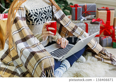 Christmas online shopping. Unrecognized woman with coffee, buy presents on laptop, prepare to xmas, among gift boxes and packages. Winter sales Christmas online shopping. Unrecognized woman with coffee, buy presents on laptop, prepare to xmas, among gift boxes and packages. Winter sales 138408871