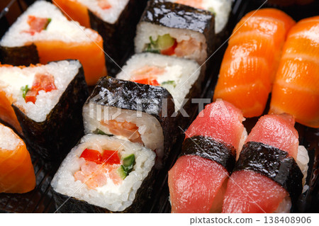 Japanese food restaurant delivery. Sushi maki and roll set closeup in black takeaway box, seafood background Japanese food restaurant delivery. Sushi maki and roll set closeup in black takeaway box, seafood background 138408906