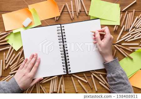 Close-up of creative designer drawing something in sketchbook at workplace. Top view flat lay shot of many blank sticky notes, color pencils on wooden table background, copy space, nobody, objects Close-up of creative designer drawing something in sketchbook at workplace. Top view flat lay shot of many blank sticky notes, color pencils on wooden table background, copy space, nobody, objects 138408911
