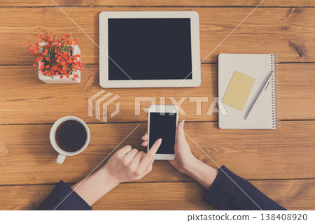 Top view table of business woman checking schedule and touching screen on phone. Freelancer working with portable computer while sitting at wooden desk at coffee shop Top view table of business woman checking schedule and touching screen on phone. Freelancer working with portable computer while sitting at wooden desk at coffee shop 138408920