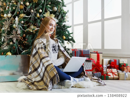 Young woman with credit card shopping online on laptop in cozy christmas interior. Girl sitting under decorated pine tree among wrapped presents. Preparing to xmas, bying on winter sales, copy space Young woman with credit card shopping online on laptop in cozy christmas interior. Girl sitting under decorated pine tree among wrapped presents. Preparing to xmas, bying on winter sales, copy space 138408922