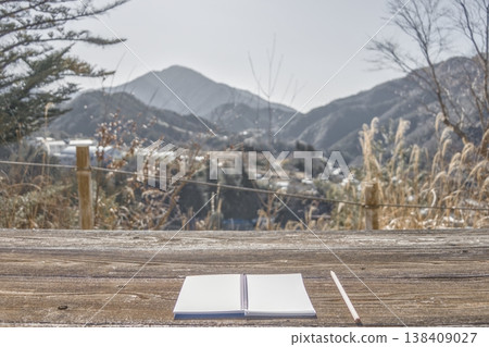A notebook and pencil on a wooden table overlooking a magnificent view of the mountains, low saturation. 138409027