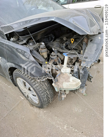 A close up side angle shows a vehicle that has crashed. The fender is bent, the headlight is broken, and parts of the engine bay are visible. This occurs on a city street after an accident. A close up side angle shows a vehicle that has crashed. The fender is bent, the headlight is broken, and parts of the engine bay are visible. This occurs on a city street after an accident. 138409119