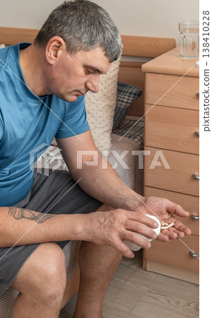 Man pouring capsules from a bottle into his hand, contemplating taking medication for illness, health problems, or insomnia at home. Man taking medicine pills for health issues 138410228