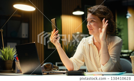 Businesswoman in the office engages in communication during virtual presentation, talking to participants about a productive collaboration. Person working late at night on a video call. Camera B. 138410628