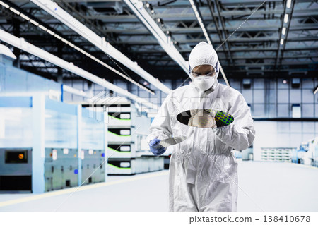 Man doing quality control on semiconductor substrates while wearing protective sterile suit in cleanroom. Specialist walking in industrial plant laboratory, assessing hardware production quality Man doing quality control on semiconductor substrates while wearing protective sterile suit in cleanroom. Specialist walking in industrial plant laboratory, assessing hardware production quality 138410678