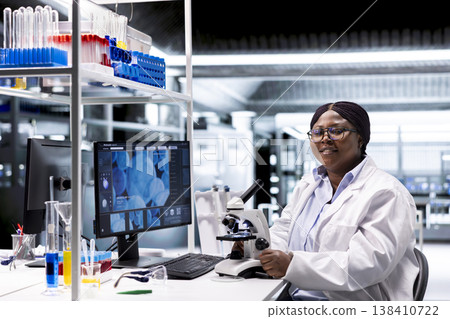 Scientist analyzing samples in laboratory setting with microscope and chemicals. Female expert advancing genetics research, combining laboratory analysis with biochemistry studies. 138410722