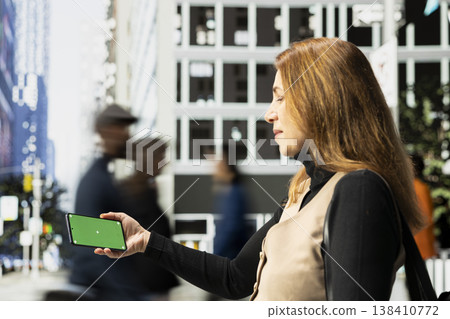 Horizontal green screen on phone held by businesswoman near urban motion of diverse pedestrians crowd on downtown street captures city life, diversity and the daily realistic routine. 138410772